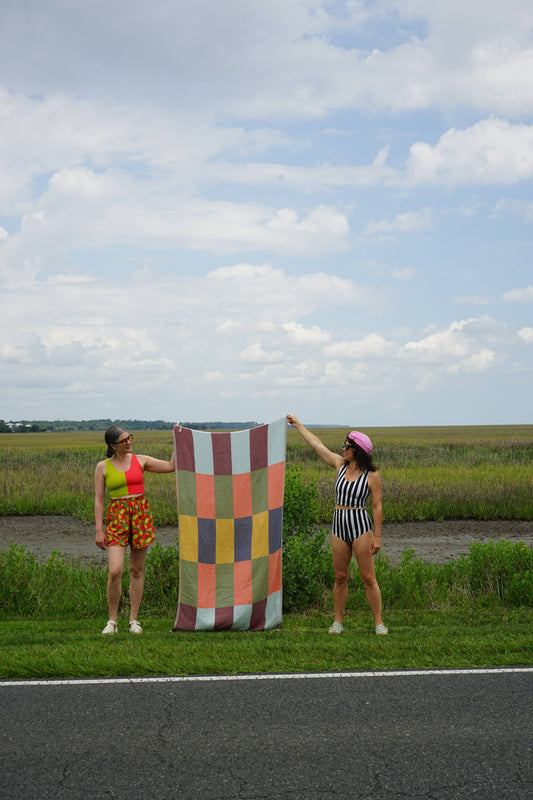 Two women holding a STATE The Label Flag Turkish Towel with a multi-colored checkered pattern outdoors