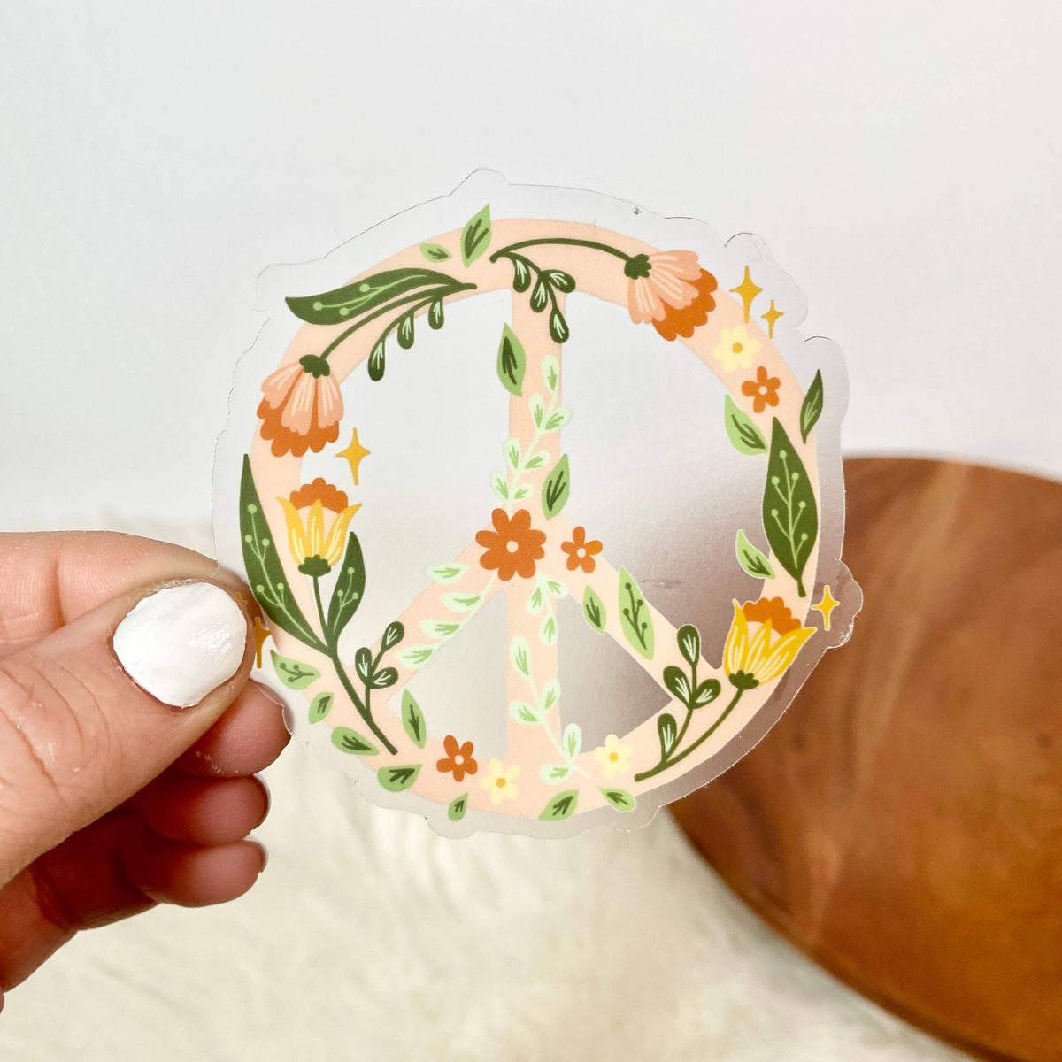 Hand holding a peace sign-shaped sticker with floral designs on a white background