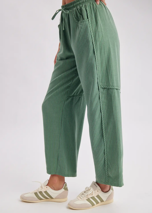 A person wearing sage green pleated wide-leg pants with a drawstring waist and cream sneakers, shown from the waist down against a plain light background.