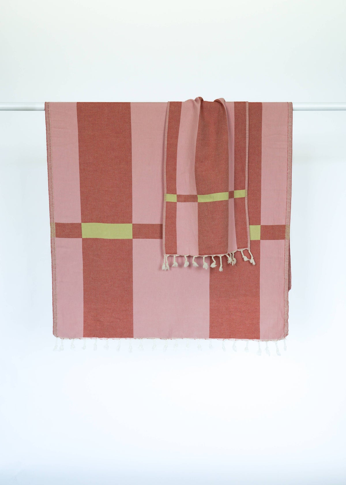 STATE The Label Fence Turkish towel in rose with a geometric block pattern and fringe detail hanging on a white rail