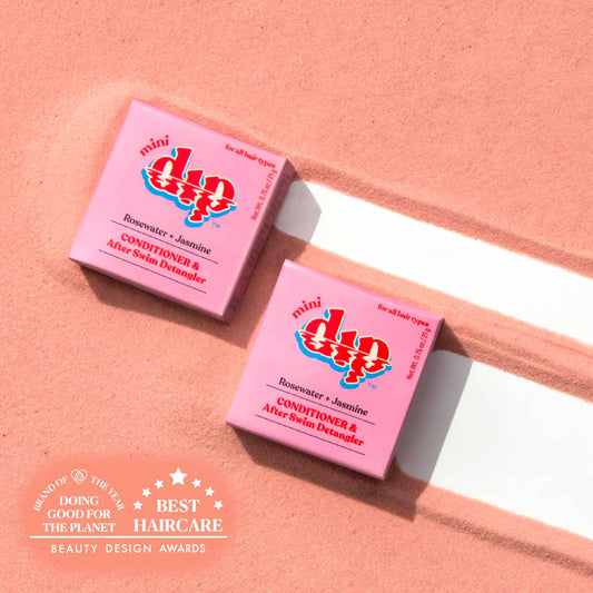 Two pink boxes of Dip Mini Rosewater and Jasmine Conditioner and After Swim Detangler on pink sand