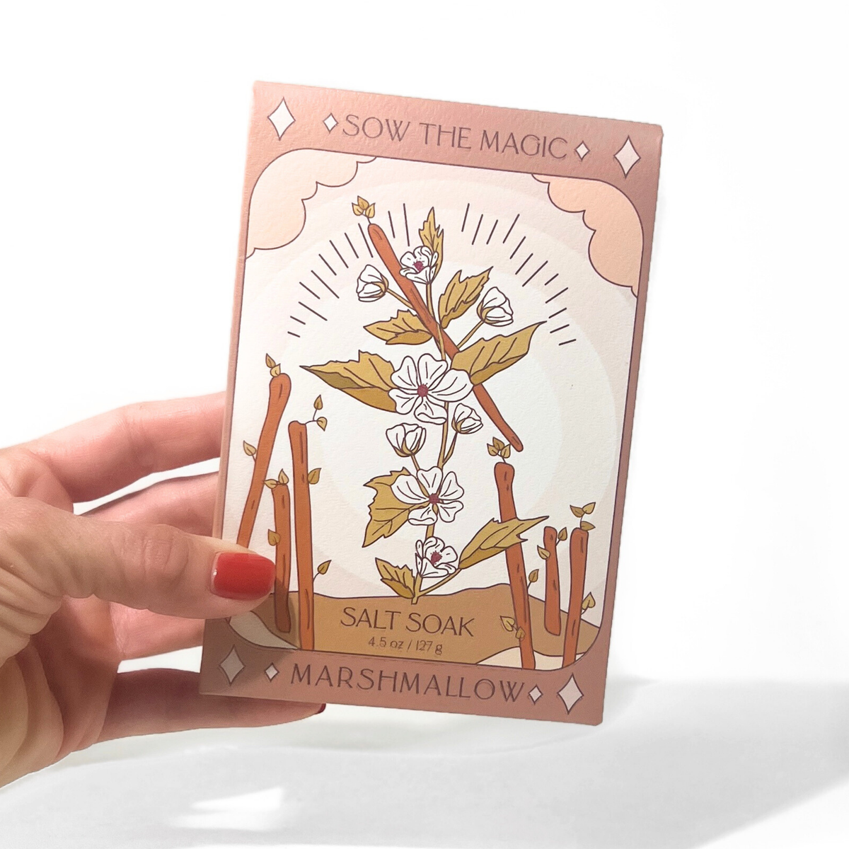 Hand holding Sow the Magic Marshmallow Tarot Salt Soak packaging with botanical illustration