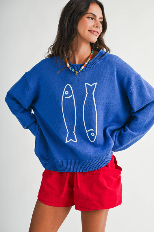 Woman wearing a blue sweater with fish designs and red shorts on a white background