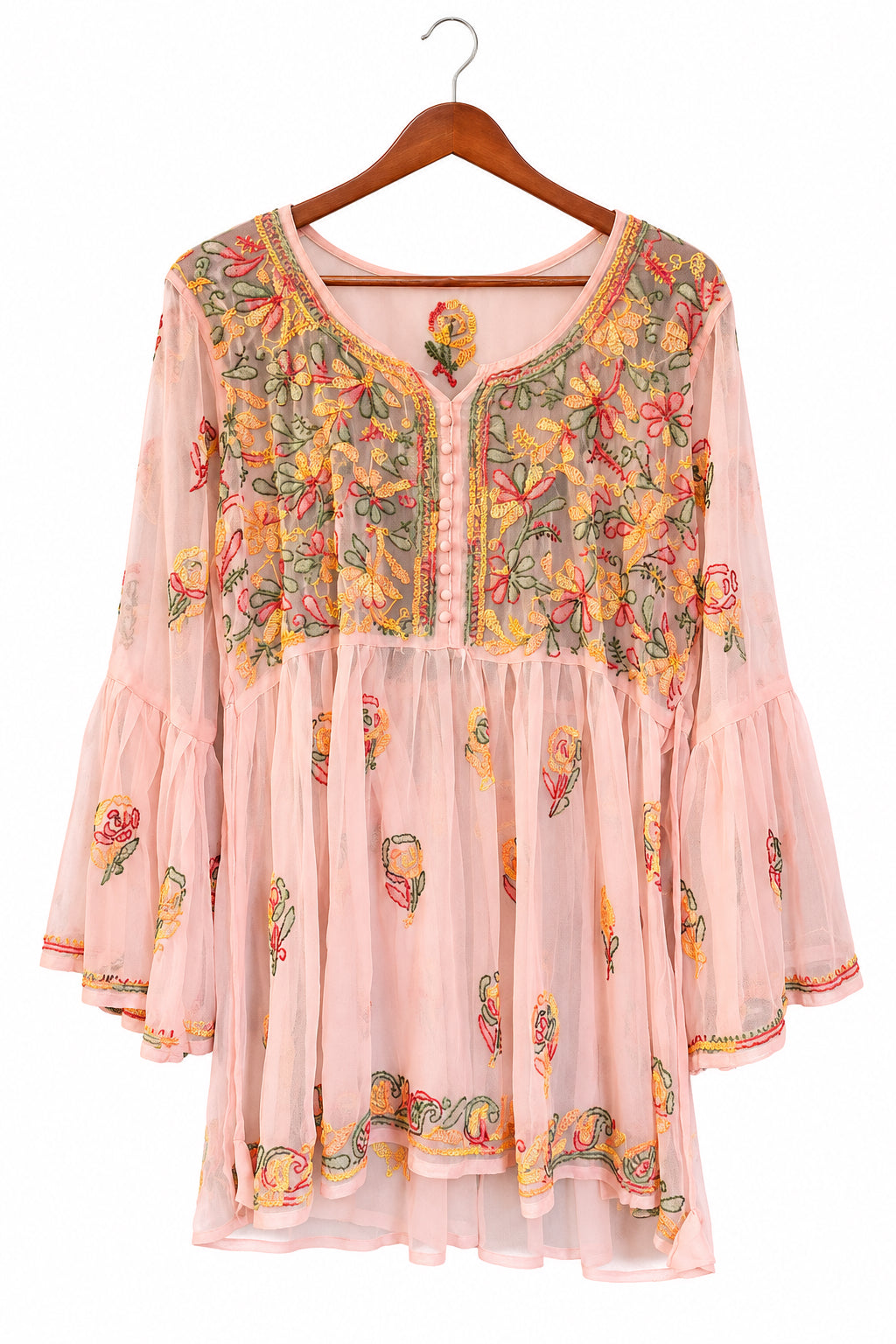 A sheer pink long-sleeve tunic top with colorful floral embroidery, hanging on a wooden hanger in front of a dark blue paneled door.
