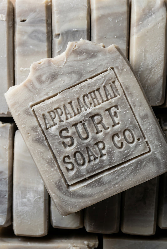 A close-up of a rectangular bar of soap with embossed Cyrillic text, resting on top of a stack of similar soap bars.