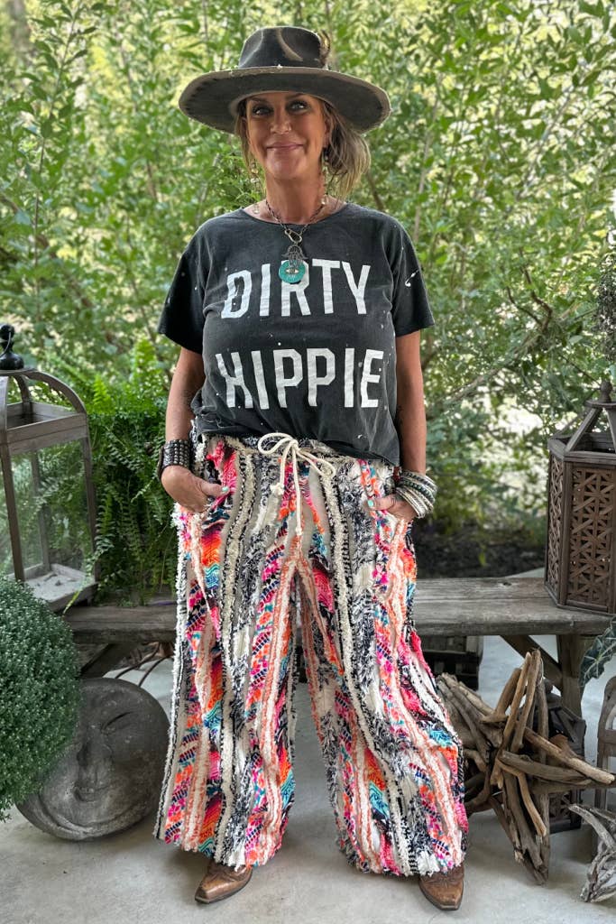 Person wearing a 'DIRTY HIPPIE' t-shirt and colorful pants standing outdoors.