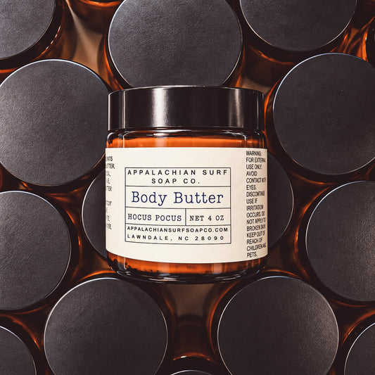 A jar of Appalachian Surf Soap Co. Body Butter with amber-colored butter visible through the glass and a black lid, centered among multiple similar jars with black lids in a repeating pattern.