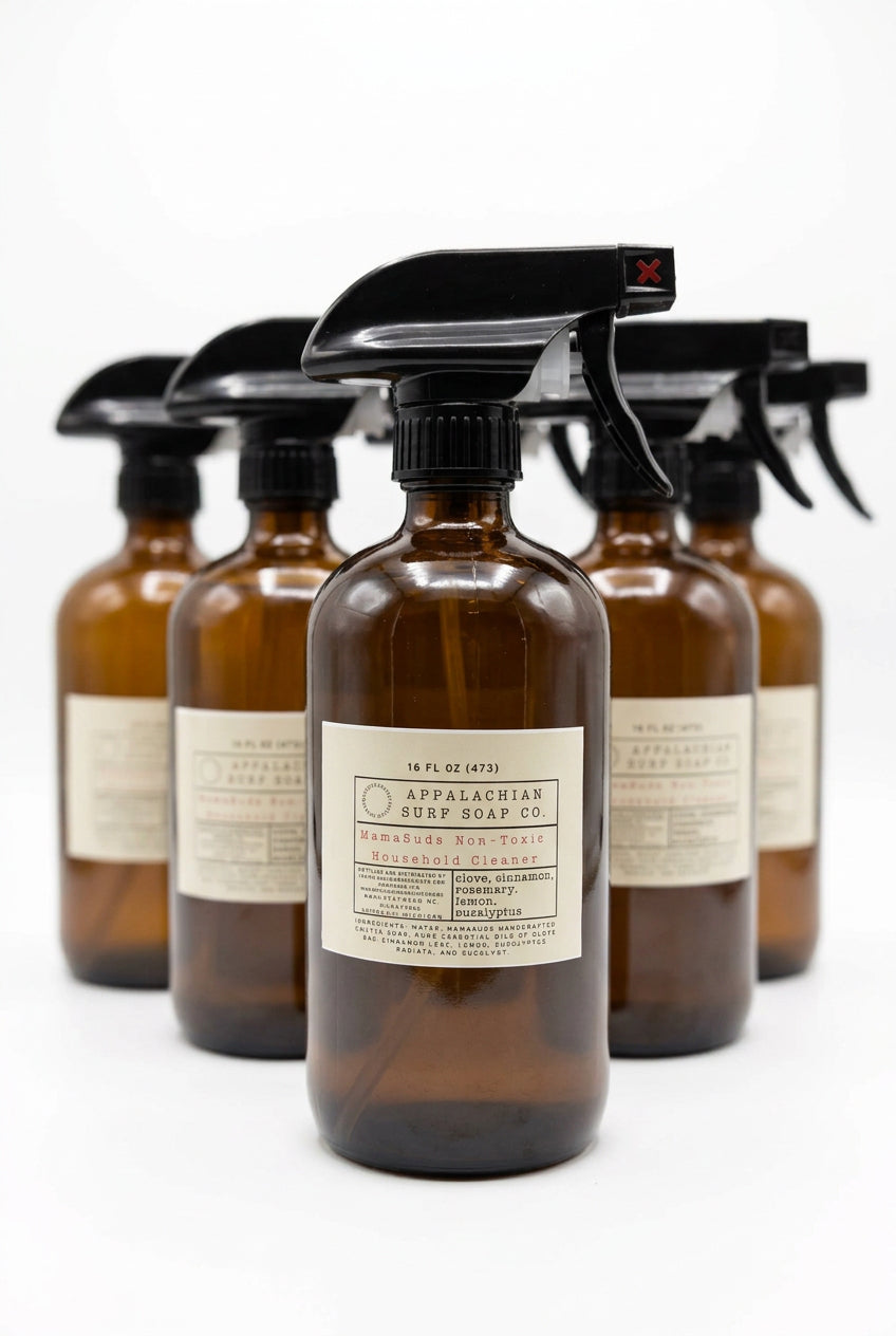 A row of amber glass spray bottles with black spray tops and cream labels, with the front bottle reading Appalachian surf soap co. set on a light surface with a blurred indoor background.