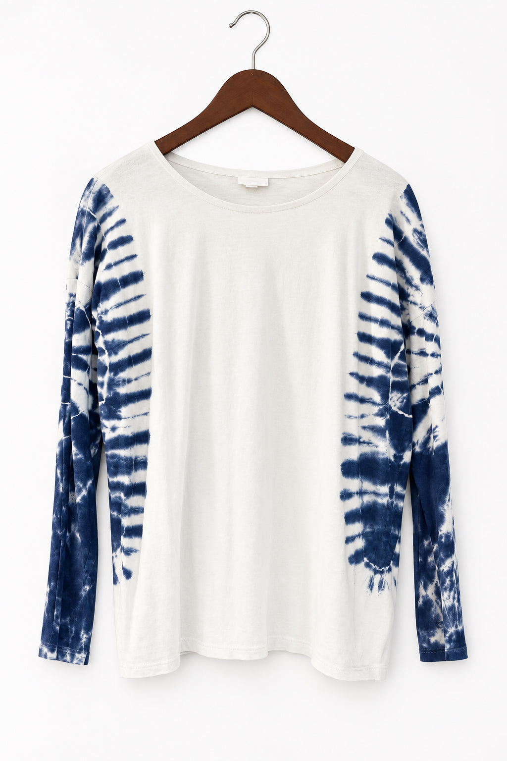 A long-sleeve tie-dye top hanging on a dark wooden hanger against a dark paneled door. The shirt has a solid off-white body with dark blue and gray tie-dye patterns on both sleeves.