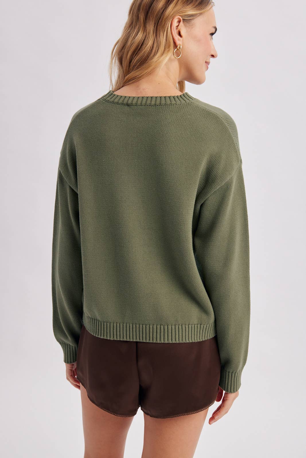 Person wearing a green sweater and brown shorts on a light gray background