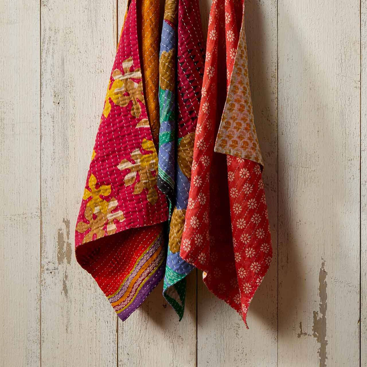 Set of three SERRV International Kantha dish towels with colorful floral and geometric patterns hanging on a wall