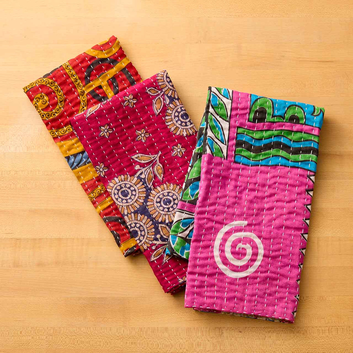 Set of three SERRV International Kantha dish towels with colorful floral and geometric patterns on a wooden surface