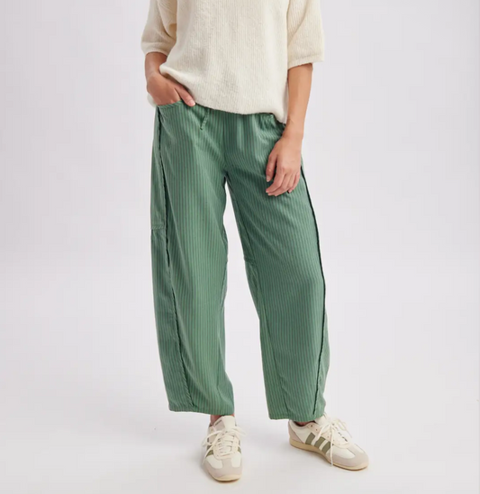 Model wearing sage green, vertically striped, wide-leg pants with a relaxed fit, elastic waistband, and side pockets, styled with a cream short-sleeve knit sweater and sneakers.