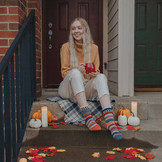 Person wearing Solmate Socks Nutmeg crew socks sitting on a porch with pumpkins and autumn leaves