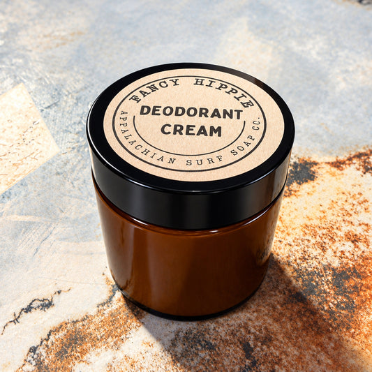 An amber glass jar of Fancy Hippie Deodorant Cream with a black lid and a beige kraft paper label, set on a textured stone surface.