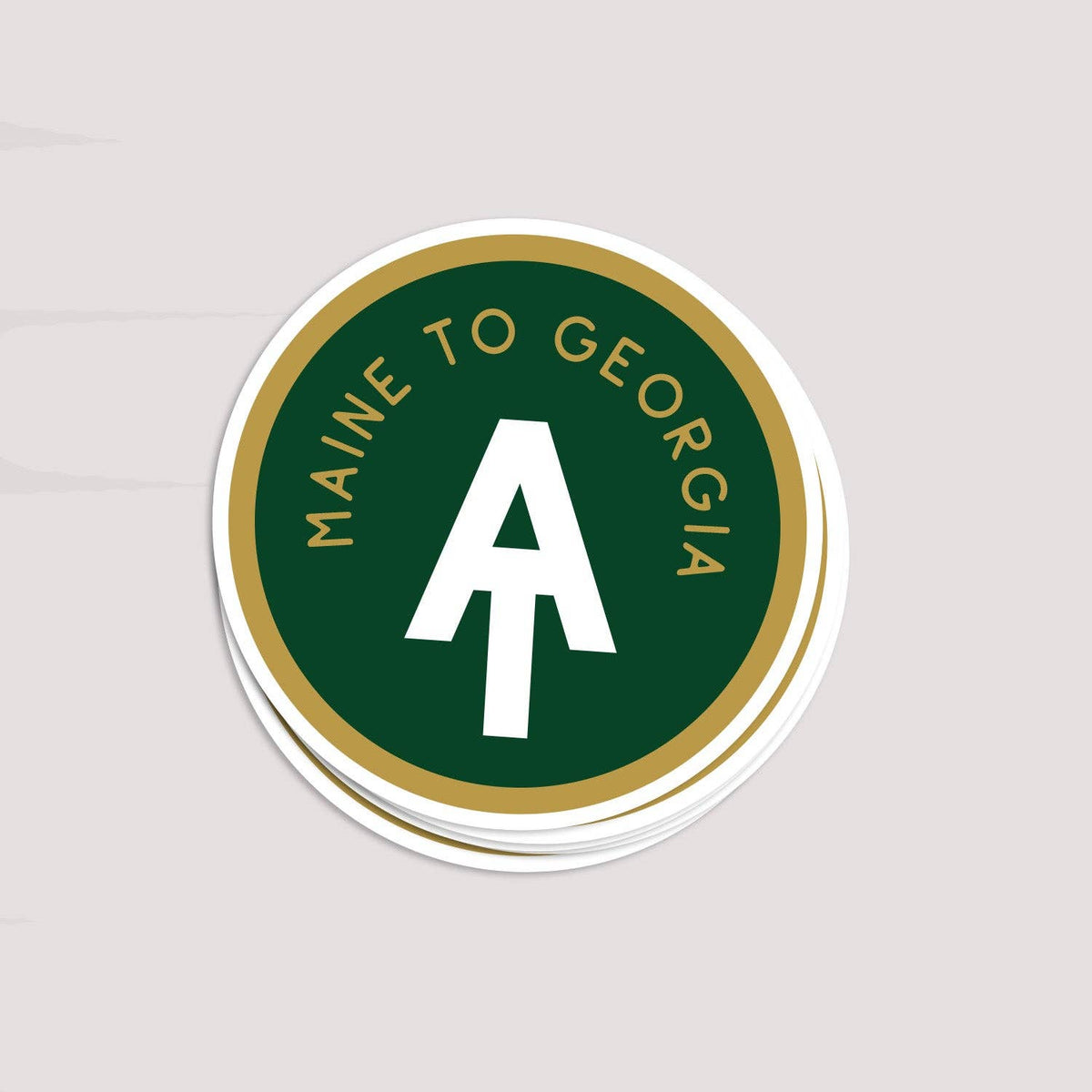 A stack of round stickers featuring a dark green center with a large white letter 'A', the words 'MAINE TO GEORGIA' in gold around the edge, and a white outer border, shown on a light gray background.