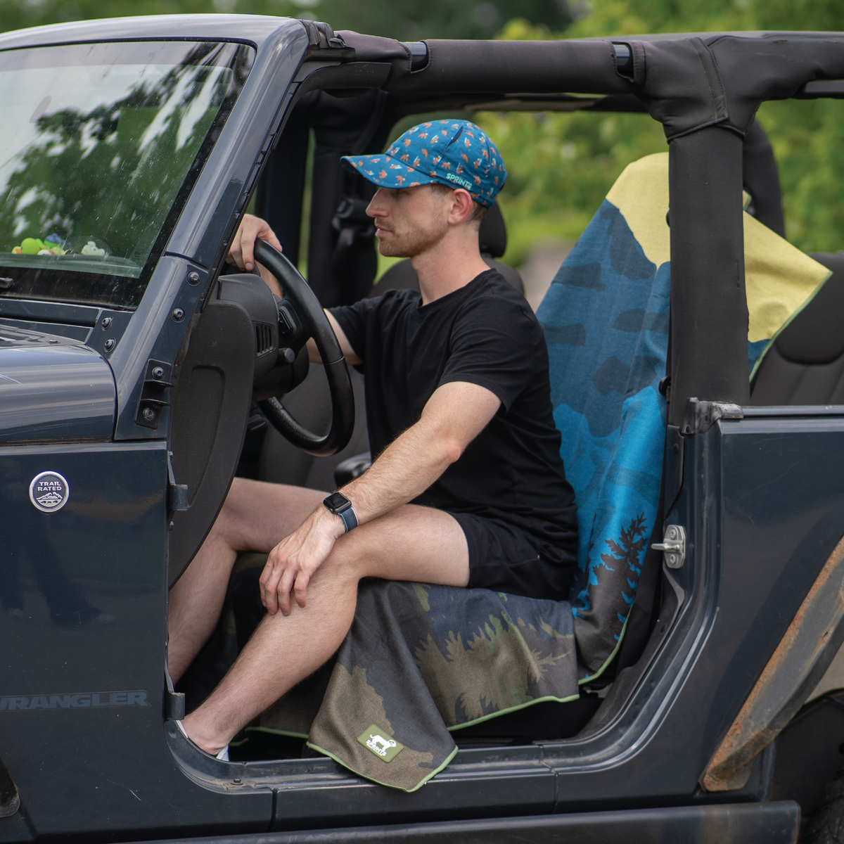 Man sitting in an open-top vehicle with a blue patterned cap and black shirt.