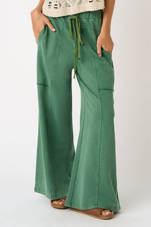 A person wearing green wide-leg drawstring pants with side pockets, paired with a cream crochet top and brown sandals, shown against a plain light background.