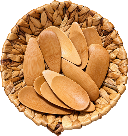 A set of light natural bamboo serving spoons arranged inside a woven straw basket on a plain white background.